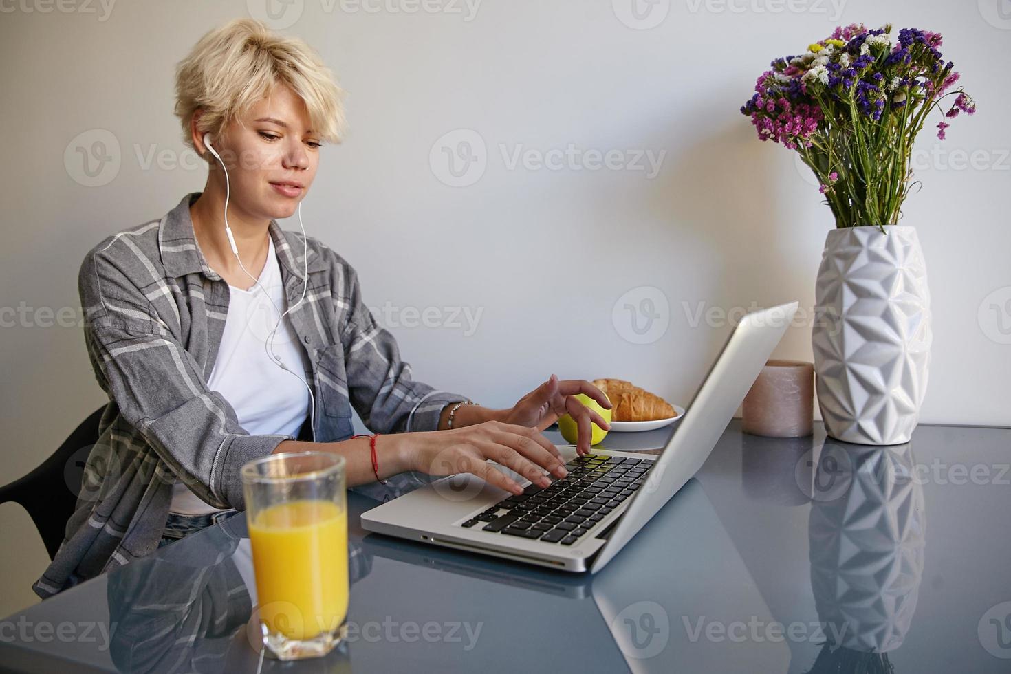 Close-up photo of attractive young blond woman with short hair, wearing casual clothes, working remotely from home, drinking orange juice, answering an e-mail