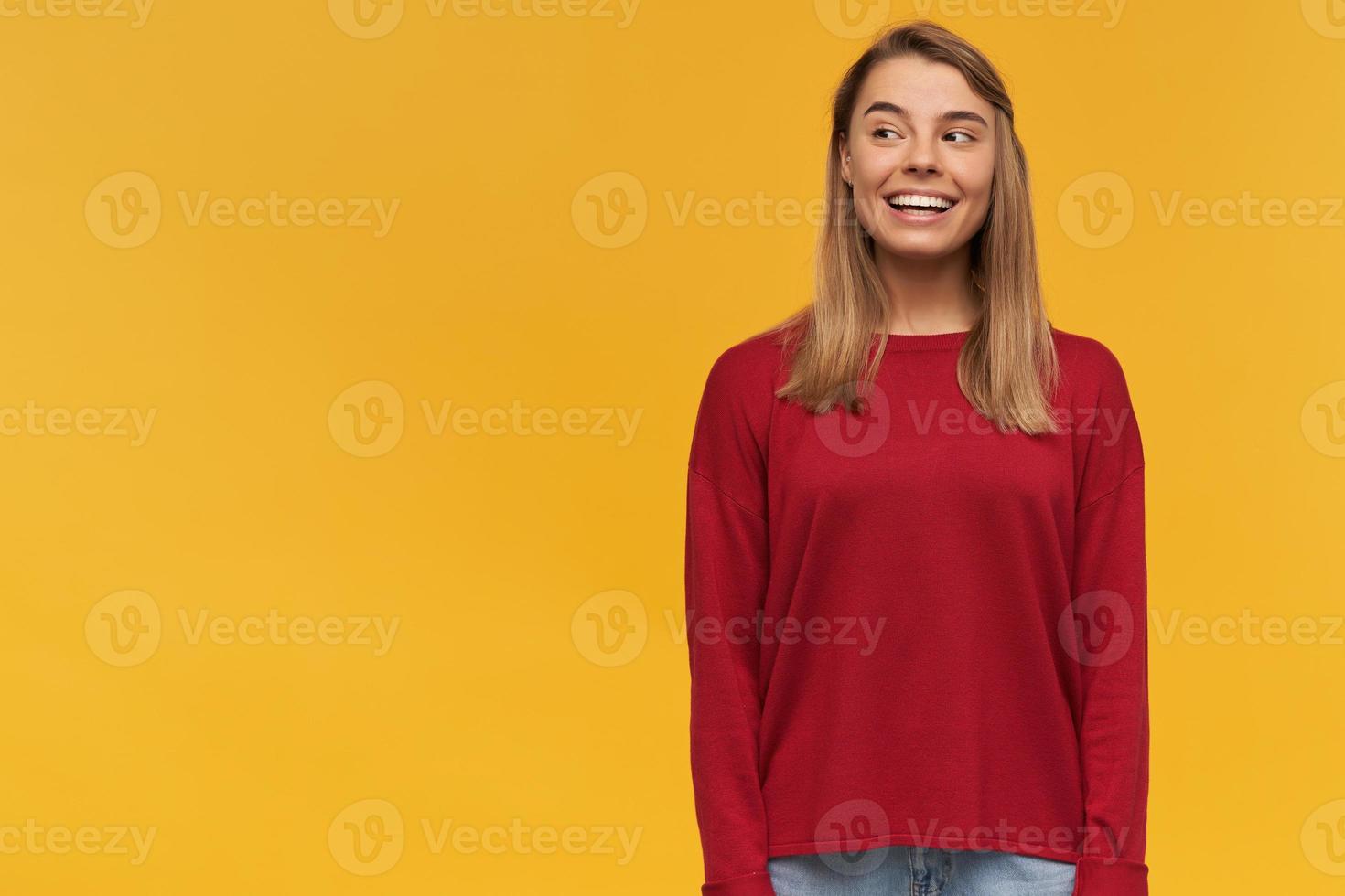Happy blonde young woman, shining from happiness, looking with curiosity interest to the left, standing on the right side, free space for text, on a yellow background photo