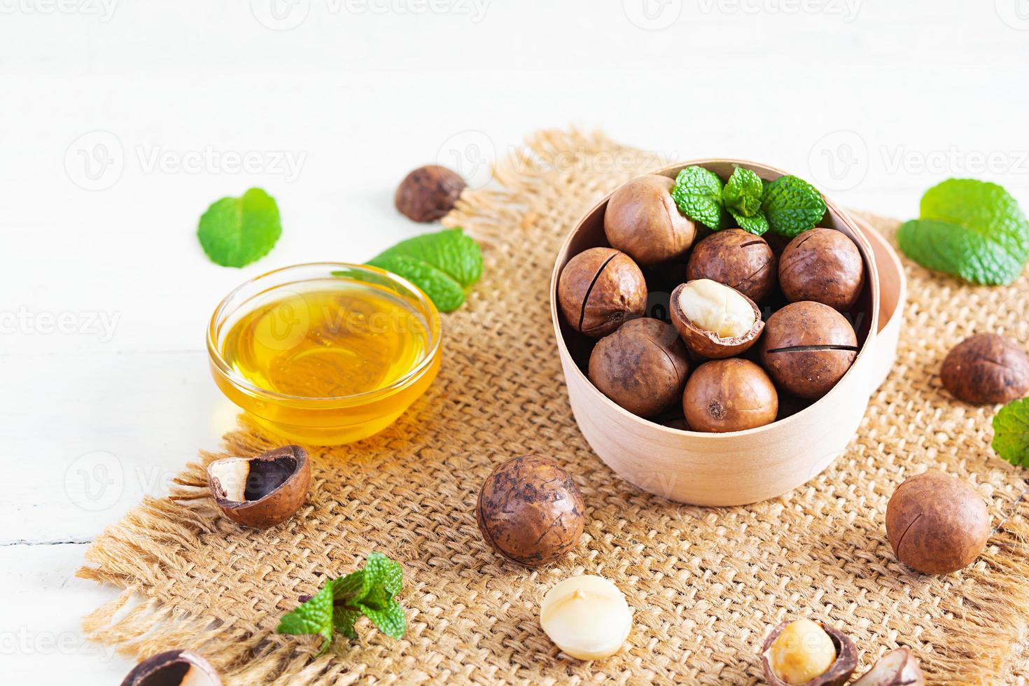 Macadamia nuts in shell with mint leaves and honey on wooden background photo