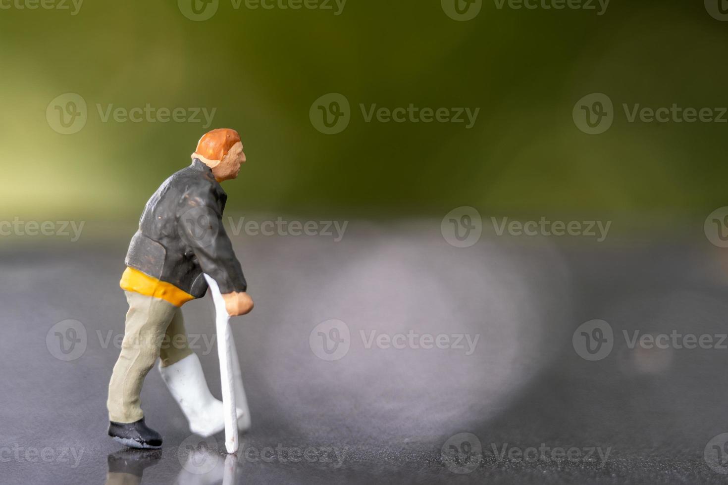 Miniature people man with broken leg is using crutch For Walking photo