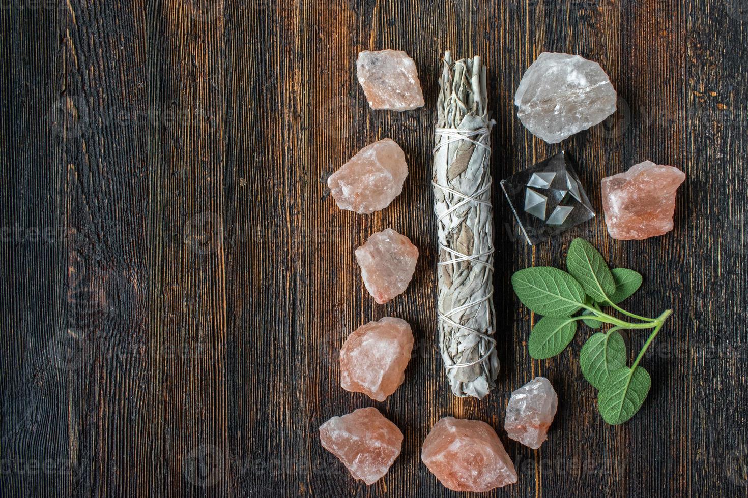 group of healing objects of smudge sage stick, pink salt crystals, and fresh sage with copy space flat lay photo