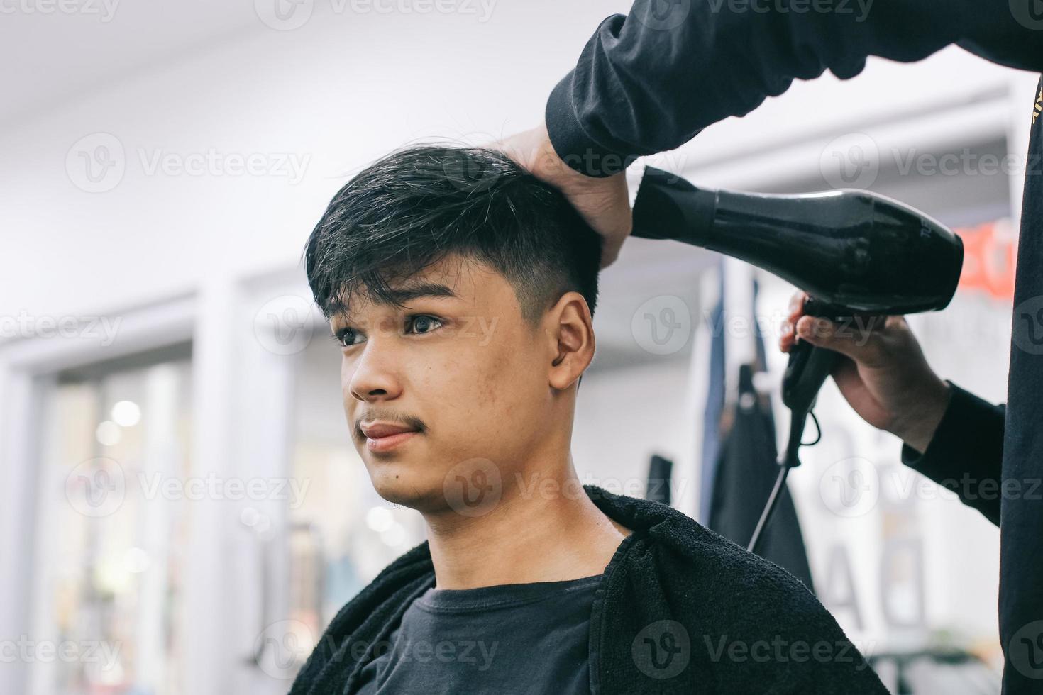 joven visitando la barbería. peluquero secando el cabello del consumidor. autocuidado, belleza masculina. Barbero. peinado moderno foto