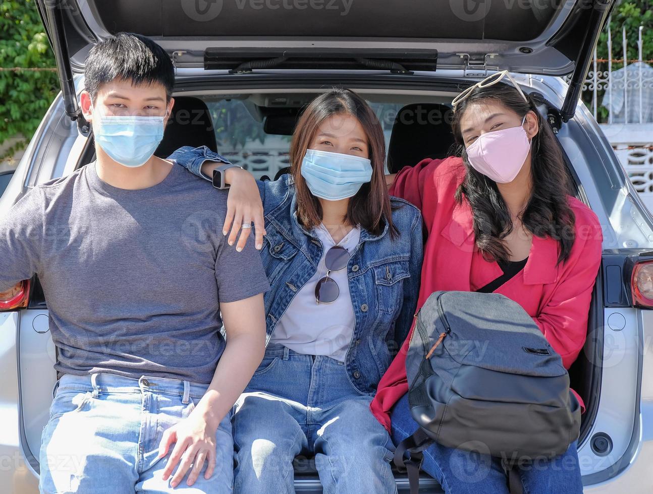 Asian young traveler friends group wearing protective mask to prevention COVID-19 and ready to go on trip by car with happy smiling face. Selective focus. photo