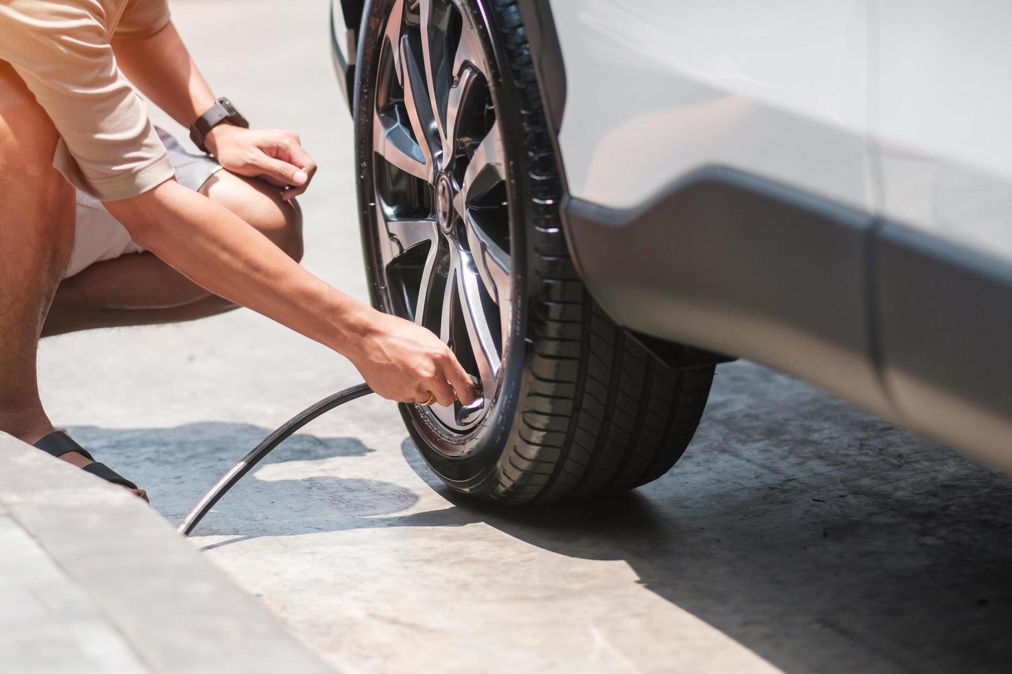 hombre conductor inflando a mano los neumáticos del vehículo, quitando la tapa de nitrógeno de la válvula del neumático para comprobar la presión del aire y llenando el aire en la rueda del coche en la gasolinera. autoservicio, mantenimiento y seguridad foto