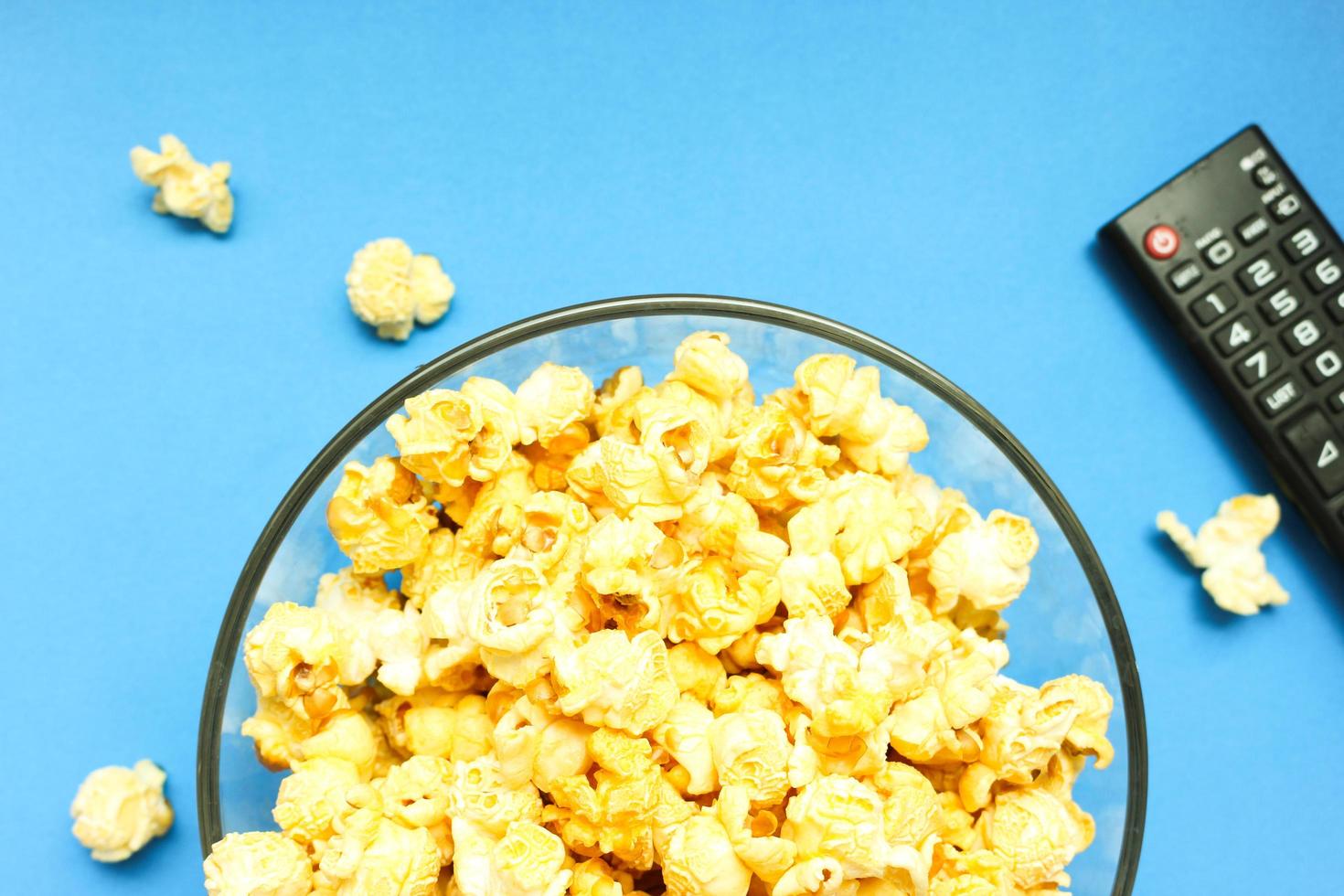 Delicious caramel popcorns sweet dessert on blue background, snacks in a glass bowl for favorite movie times. photo