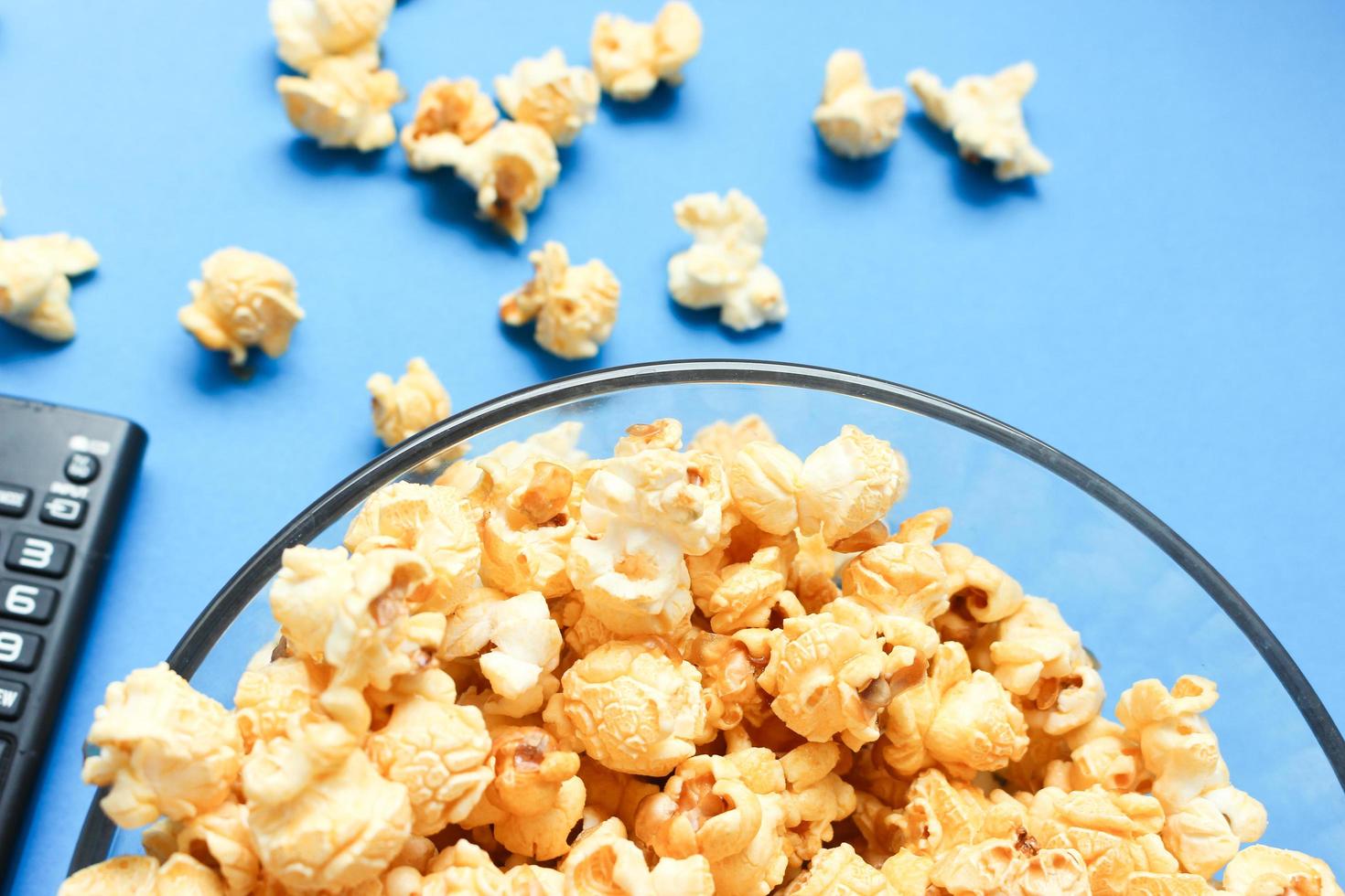 Delicious caramel popcorns sweet dessert on blue background, snacks in a glass bowl for favorite movie times. photo