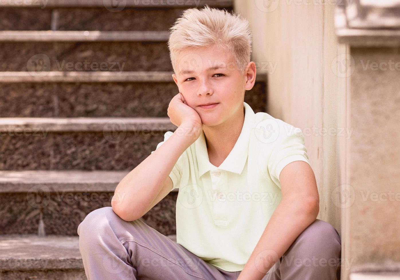 portrait of cute handsome blonde eleven old boy sitting on the stairs outdoor. Growing up, childhood, separating concept photo