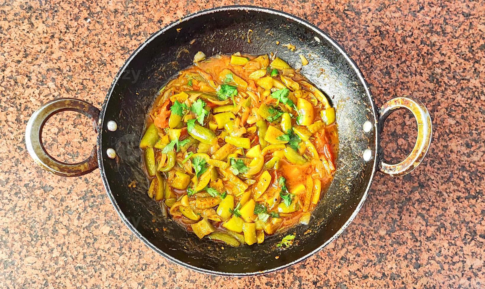 Parwal curry - Pointed gourd curry - in black wok on brown background photo