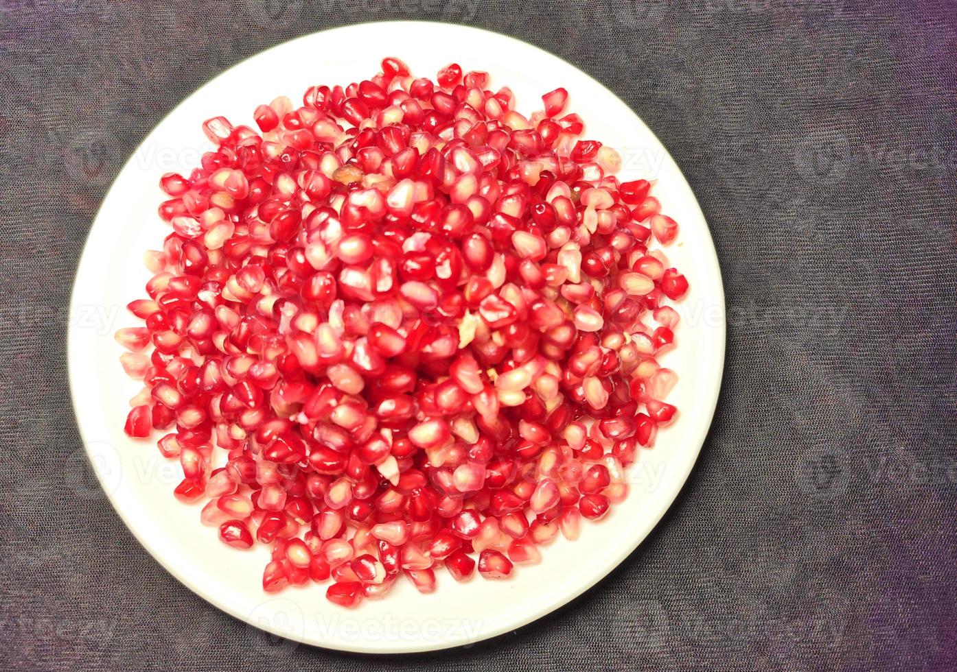 Pomegranate seeds placed on a white plate on a dark background photo