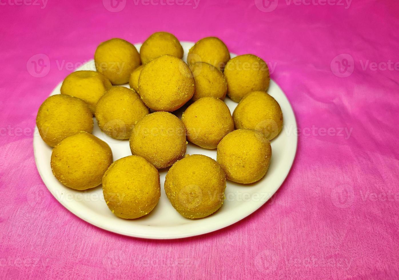 festival indio dulce - besan laddu, hecho con harina de gramo, azúcar y ghee, colocado en un plato blanco sobre un fondo de color. foto