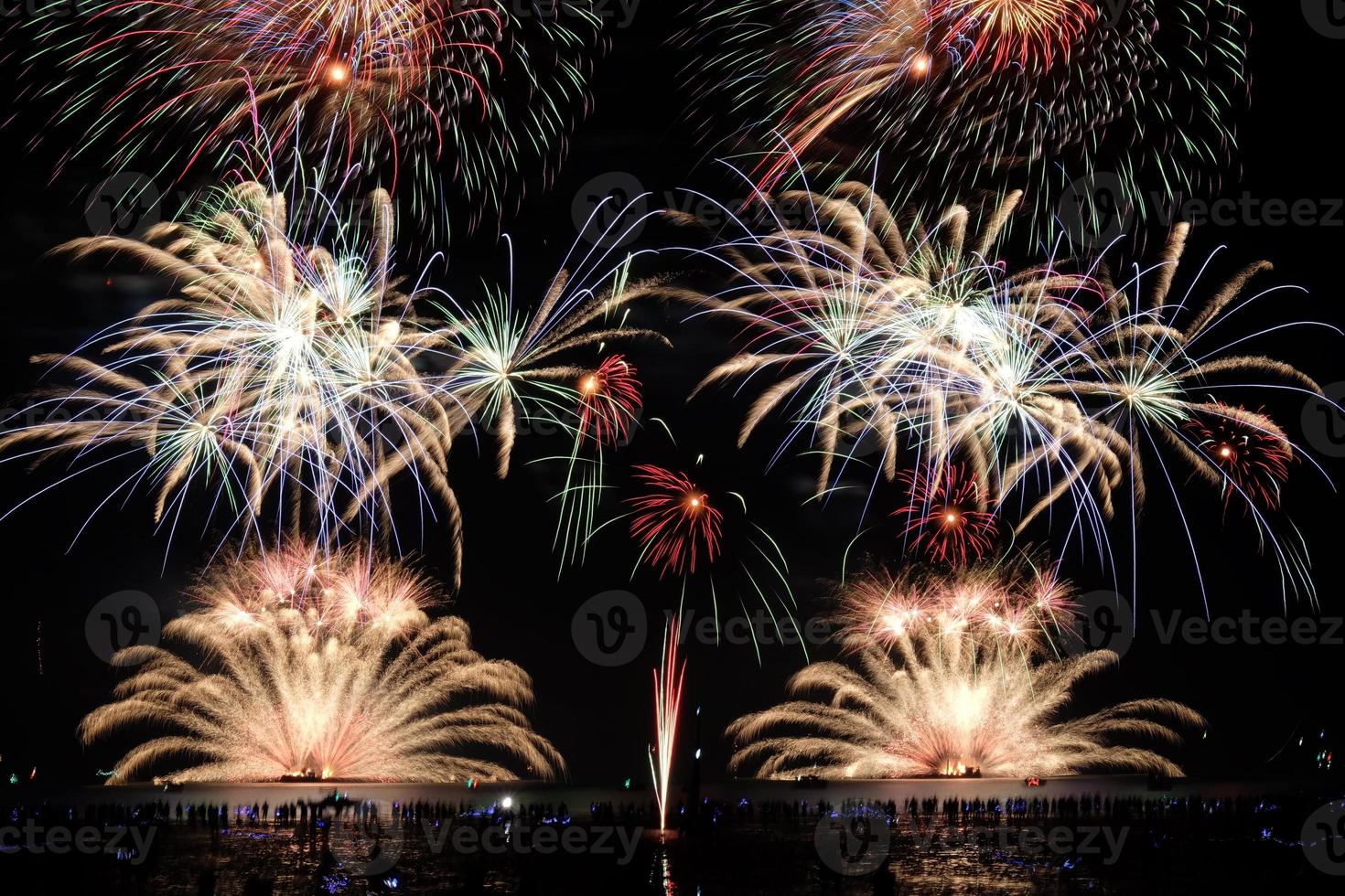 Festive fireworks display light up over night sky at the beach. Colorful firework celebration on dark background. photo