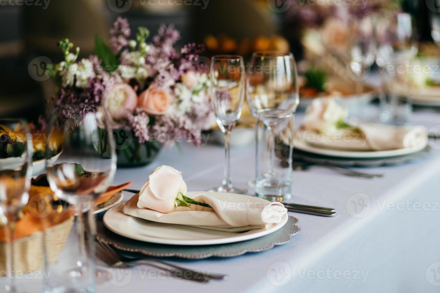 Table served for special occasion. Empty plate, glasses, forks, napkin and flowers on table covered with white tableclothes. Elegant dinner table. White table setting photo