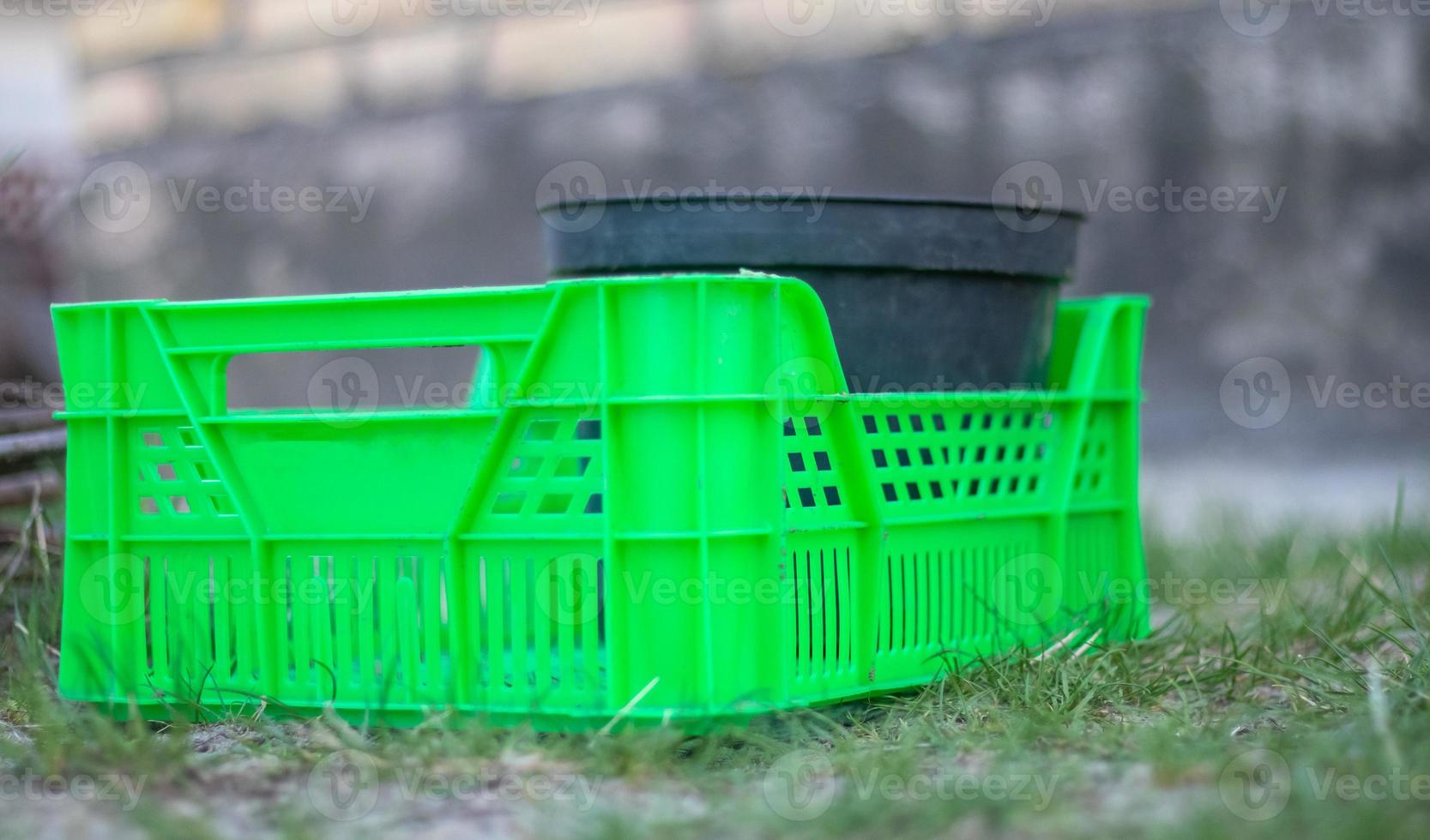 Plastic empty green box in the garden for plants or harvesting. On a sunny day in early spring. Gardening concept. Household crop collection and storage box standing in the backyard. photo