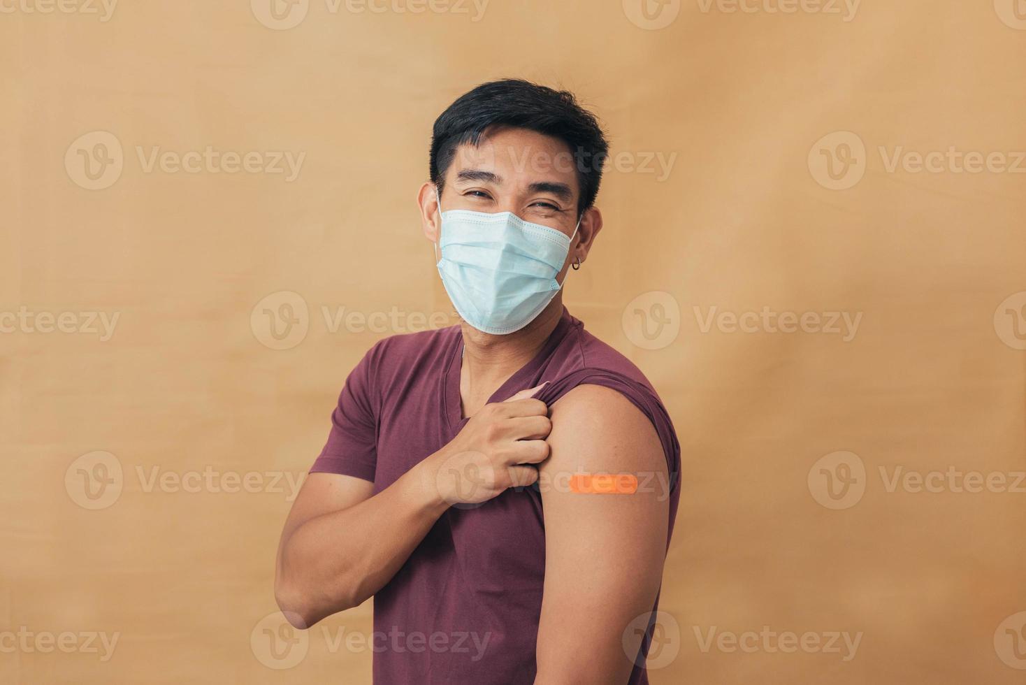 Asian man showing shoulders after getting a vaccine. Happy man showing arm with band-aids on after vaccine injection. photo