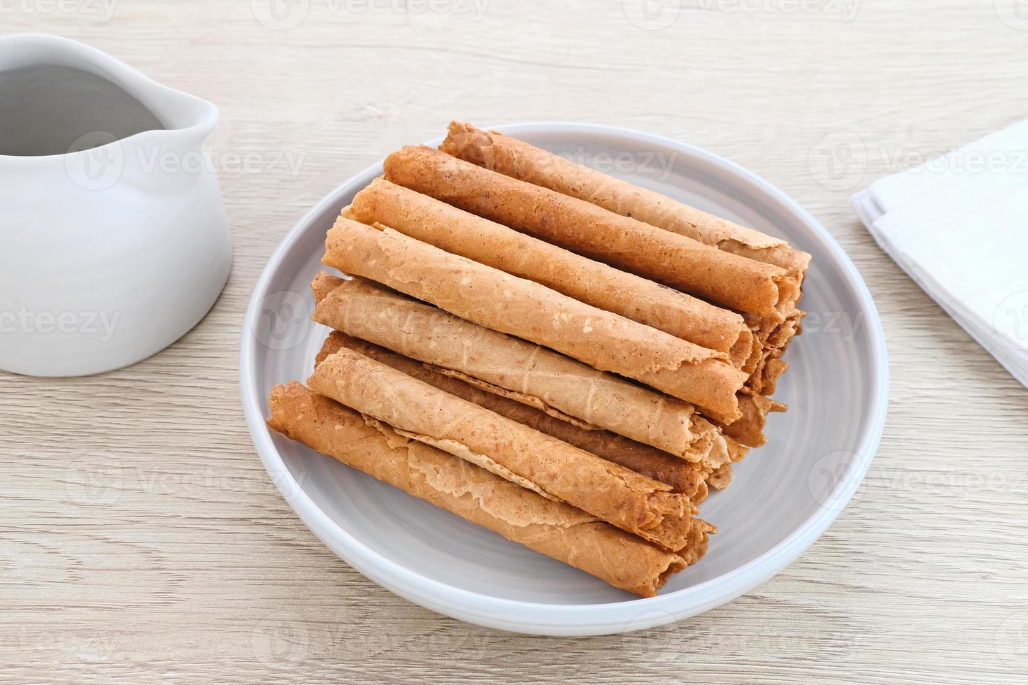 Waffle egg rolls or semprong cake, a traditional Indonesian snack with a unique shape like a layered pipe, served on a white plate. Selected focus. photo