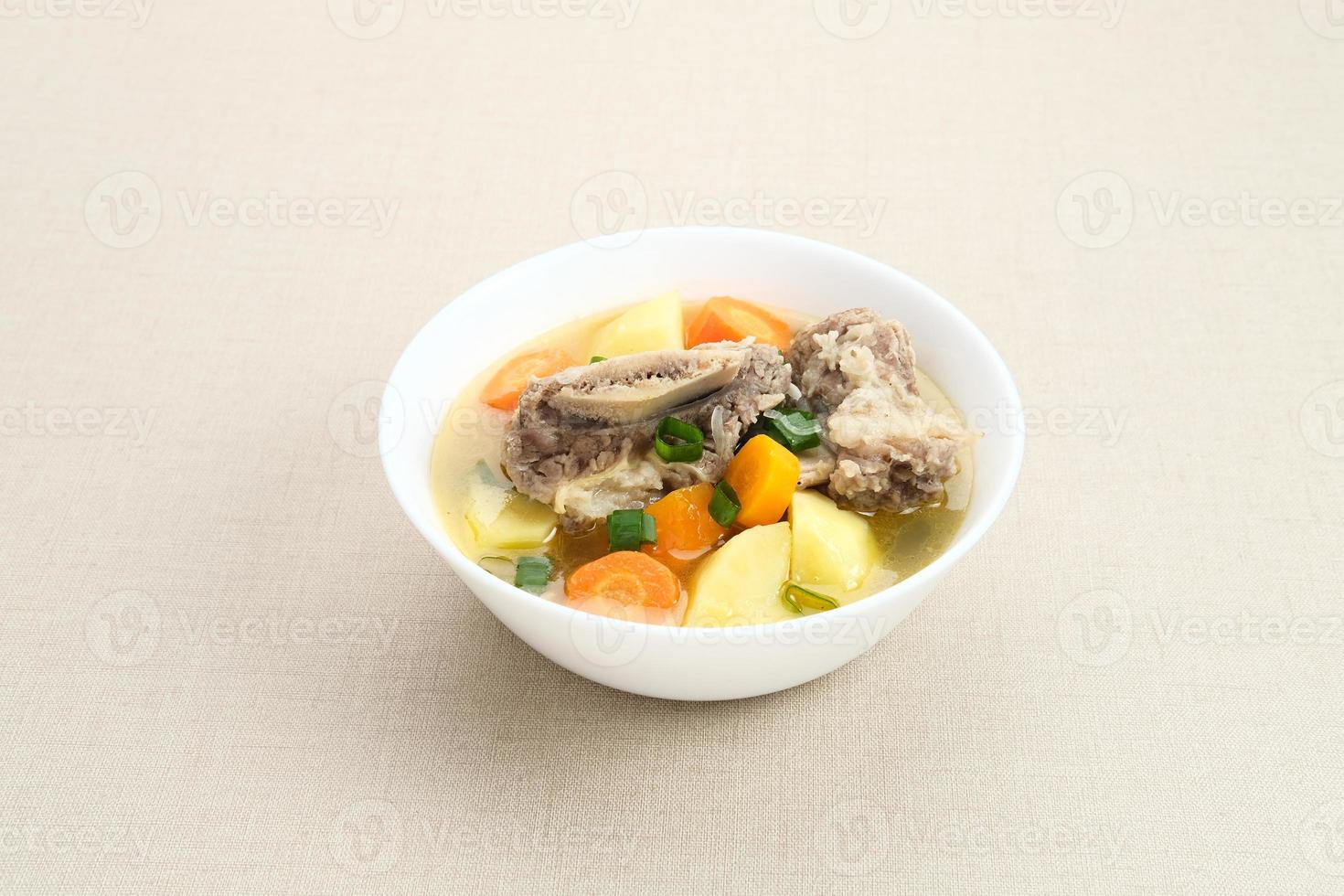 Sop Iga, Beef ribs soup, is Indonesian soup. Made from ribs, carrots, leeks, and potatoes. Served in white bowl. Selected focus photo