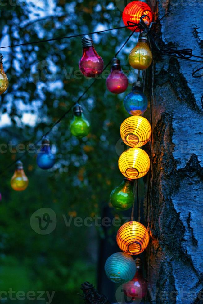 cadena de luces colgando del árbol. fiesta de jardin. Lugar romantico. luz de colores foto