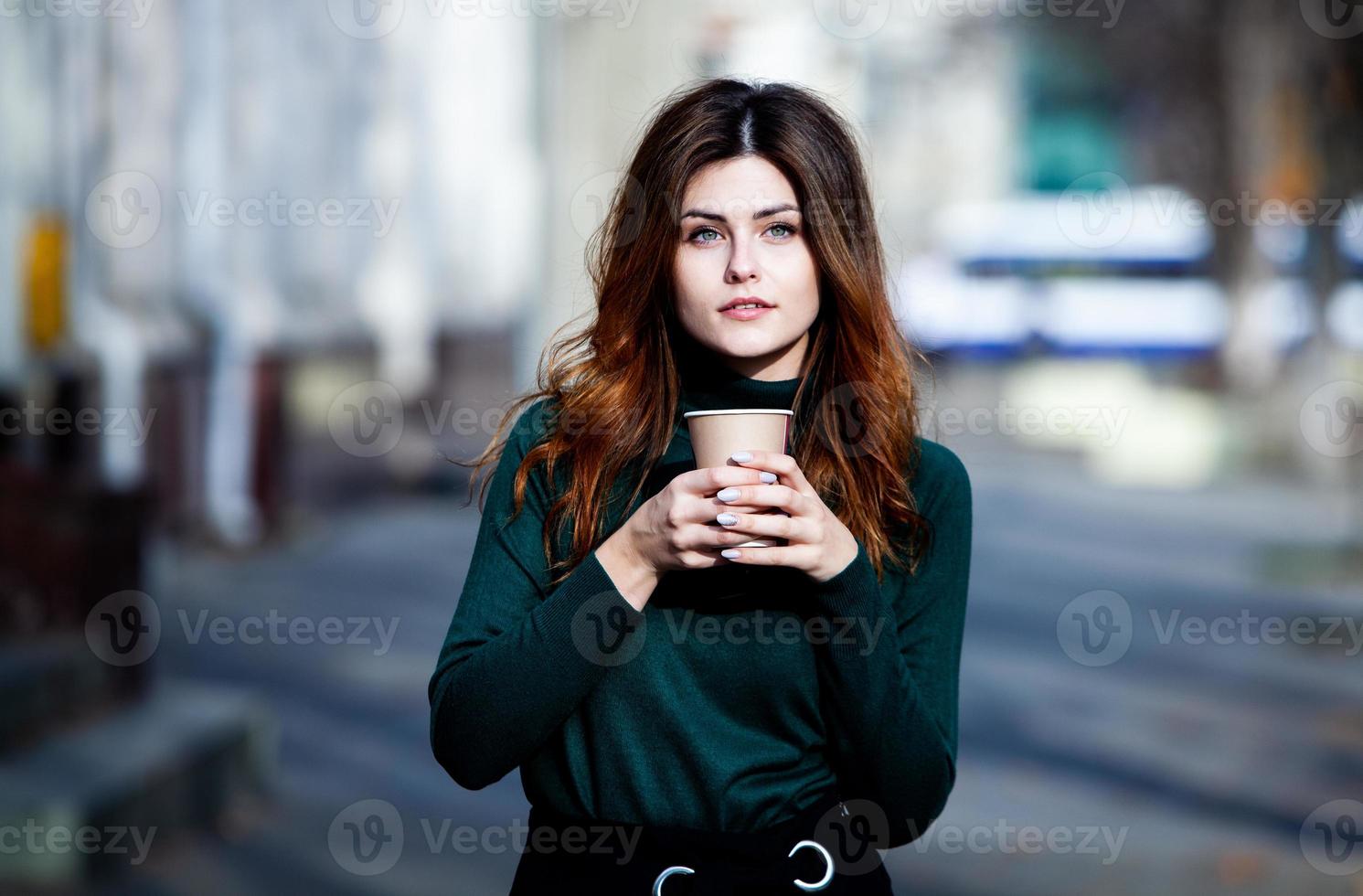 Young stylish woman drinking tea in a city street. Hipster european girl with latte paper glass. Gorgeous young woman with cup of coffee in city street. Coffee break. Coffee to go. photo