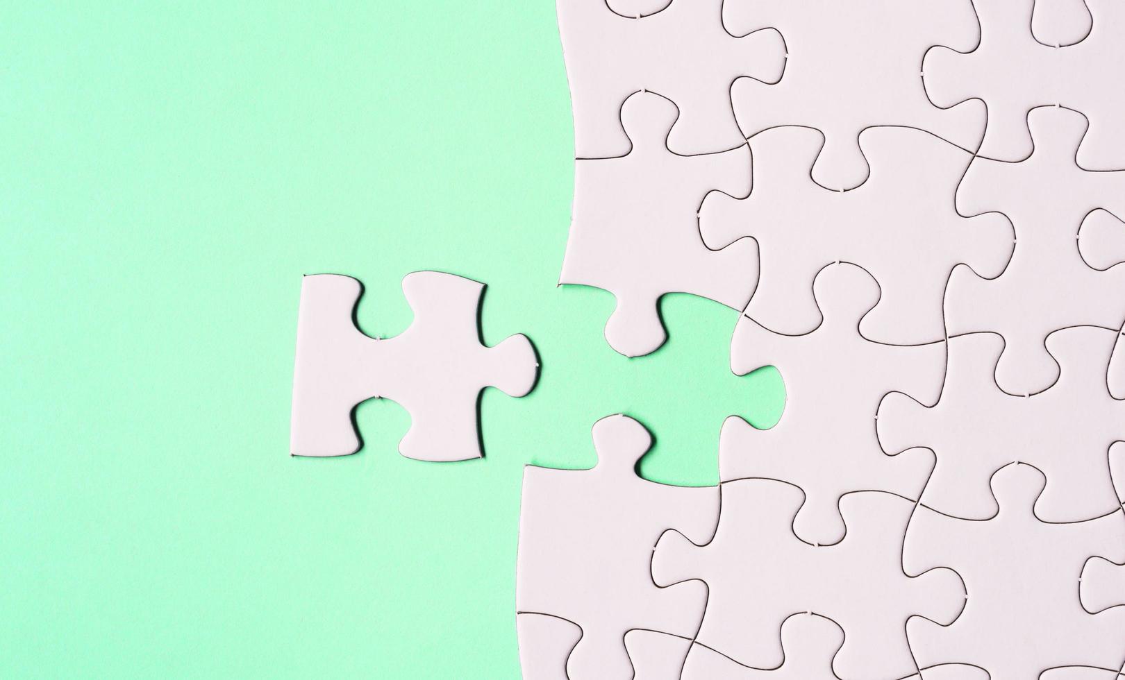 White jigsaw puzzle with some missing pieces on green background. Flat lay. photo