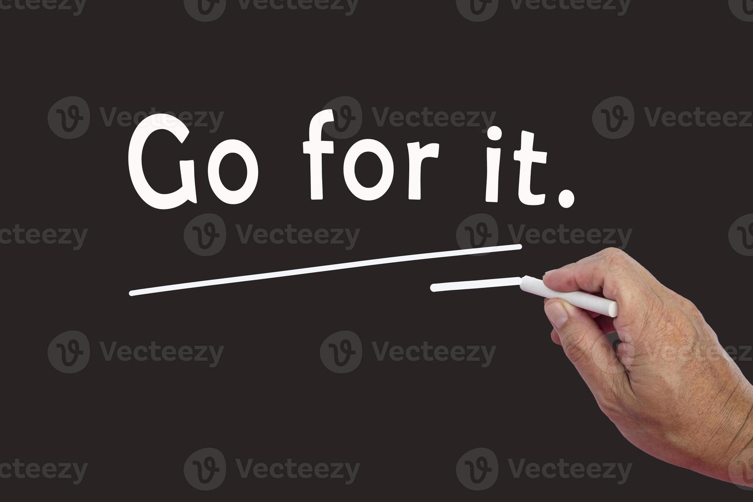 Male hand writes in white chalk pencil the word Go For It on a black background. photo