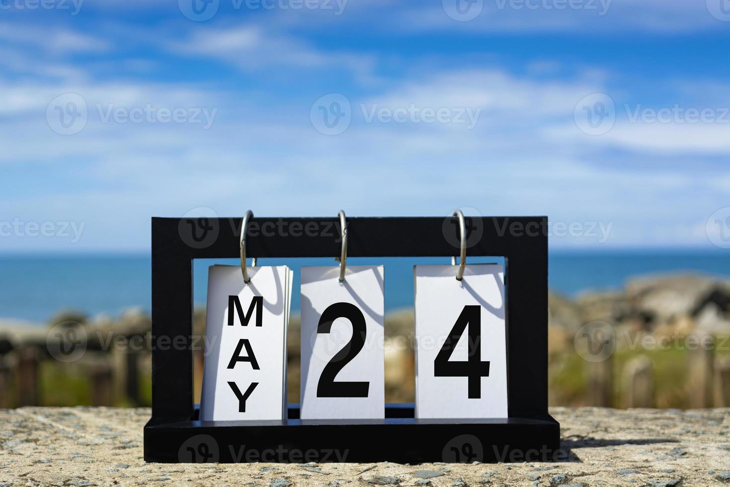 24 de mayo texto de fecha de calendario en marco de madera con fondo borroso del océano. foto