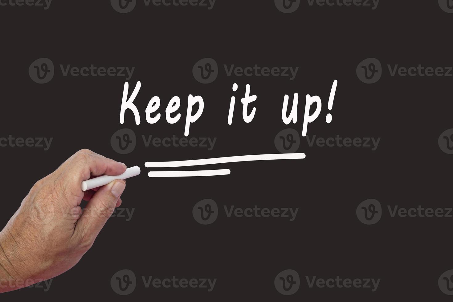 Male hand writes in white chalk pencil the word KEEP IT UP on a black background photo