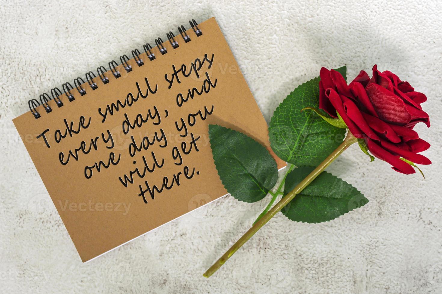Motivational and inspirational quote on brown note book with red roses on marble desk photo