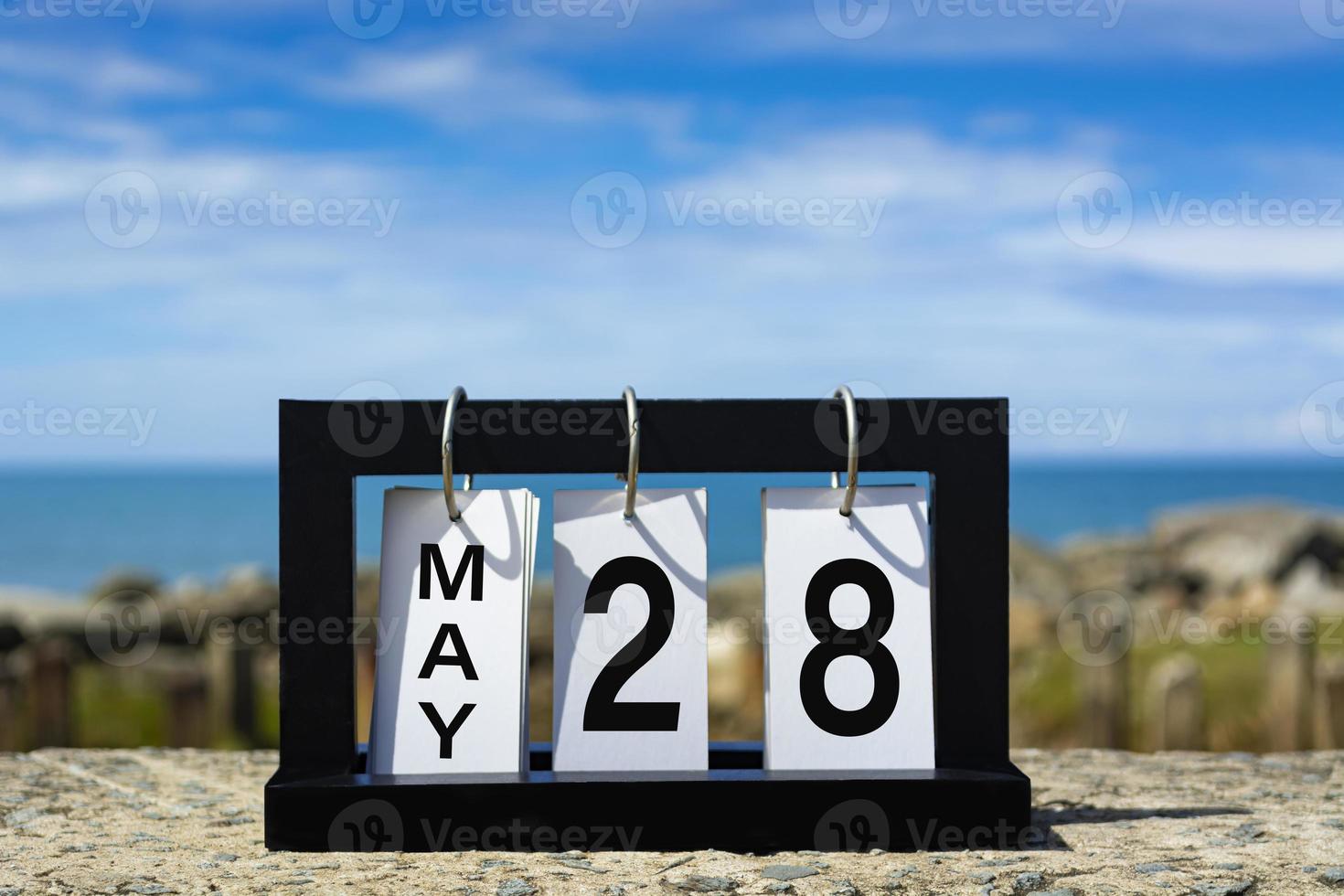 28 de mayo texto de fecha de calendario en marco de madera con fondo borroso del océano. foto