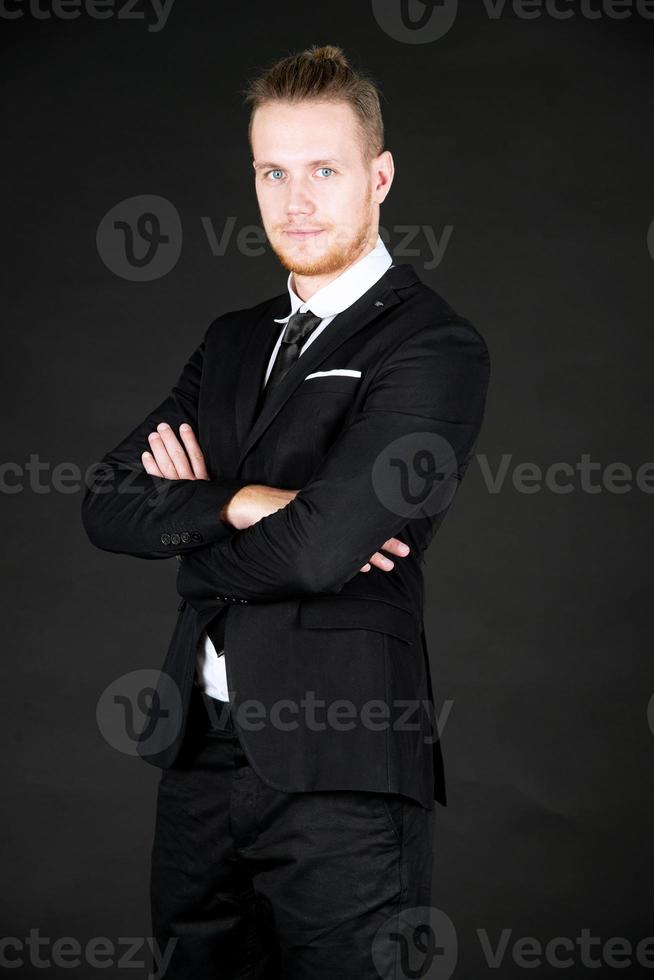 retrato de un joven hombre de negocios inteligente y guapo con traje negro parado en un fondo negro aislado. foto