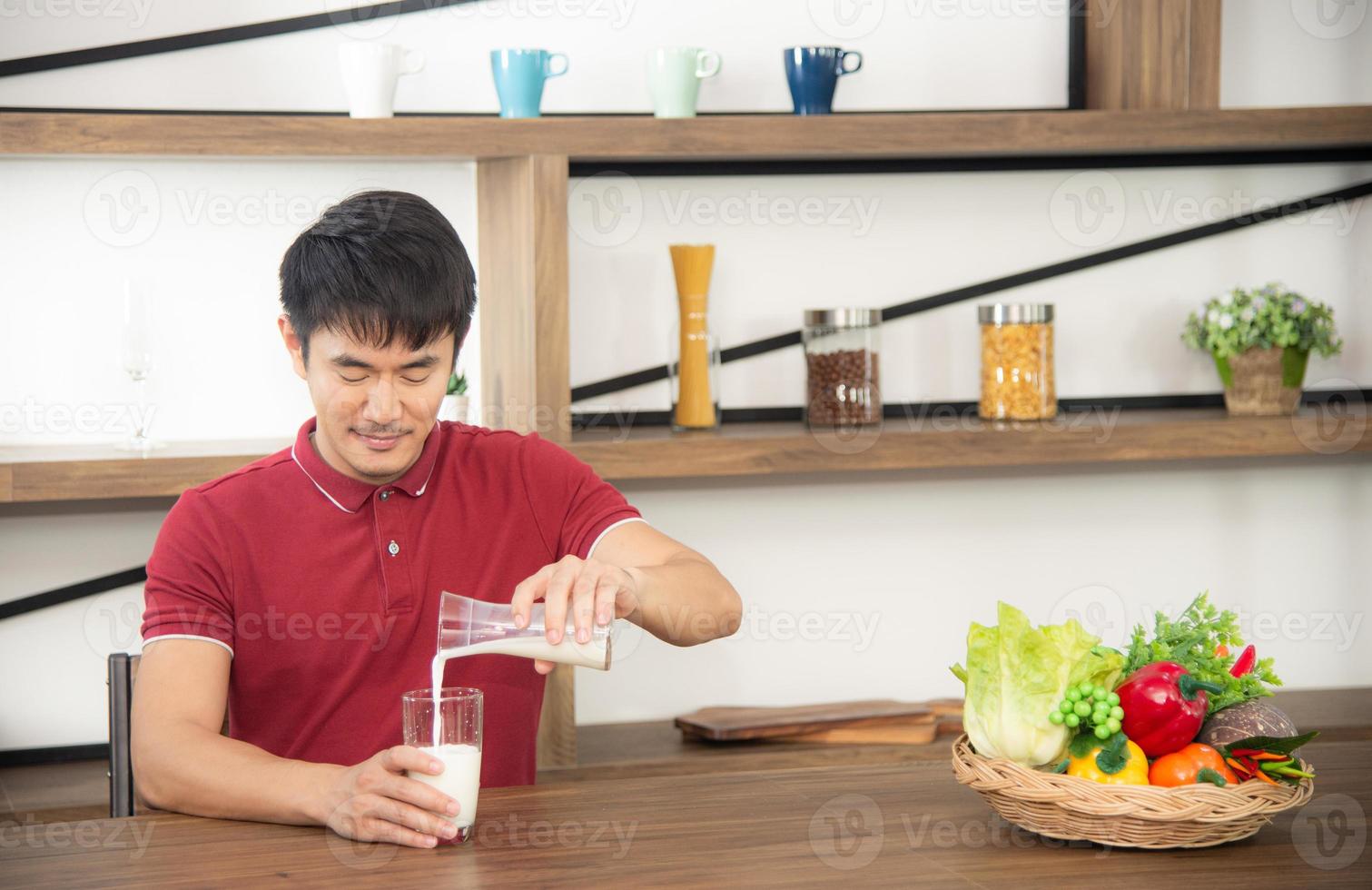 Asian syoung man with casual  red t-shirt enjoy having breakfast, drinking milk. Young man cooking food  in the loft style kitchen room photo