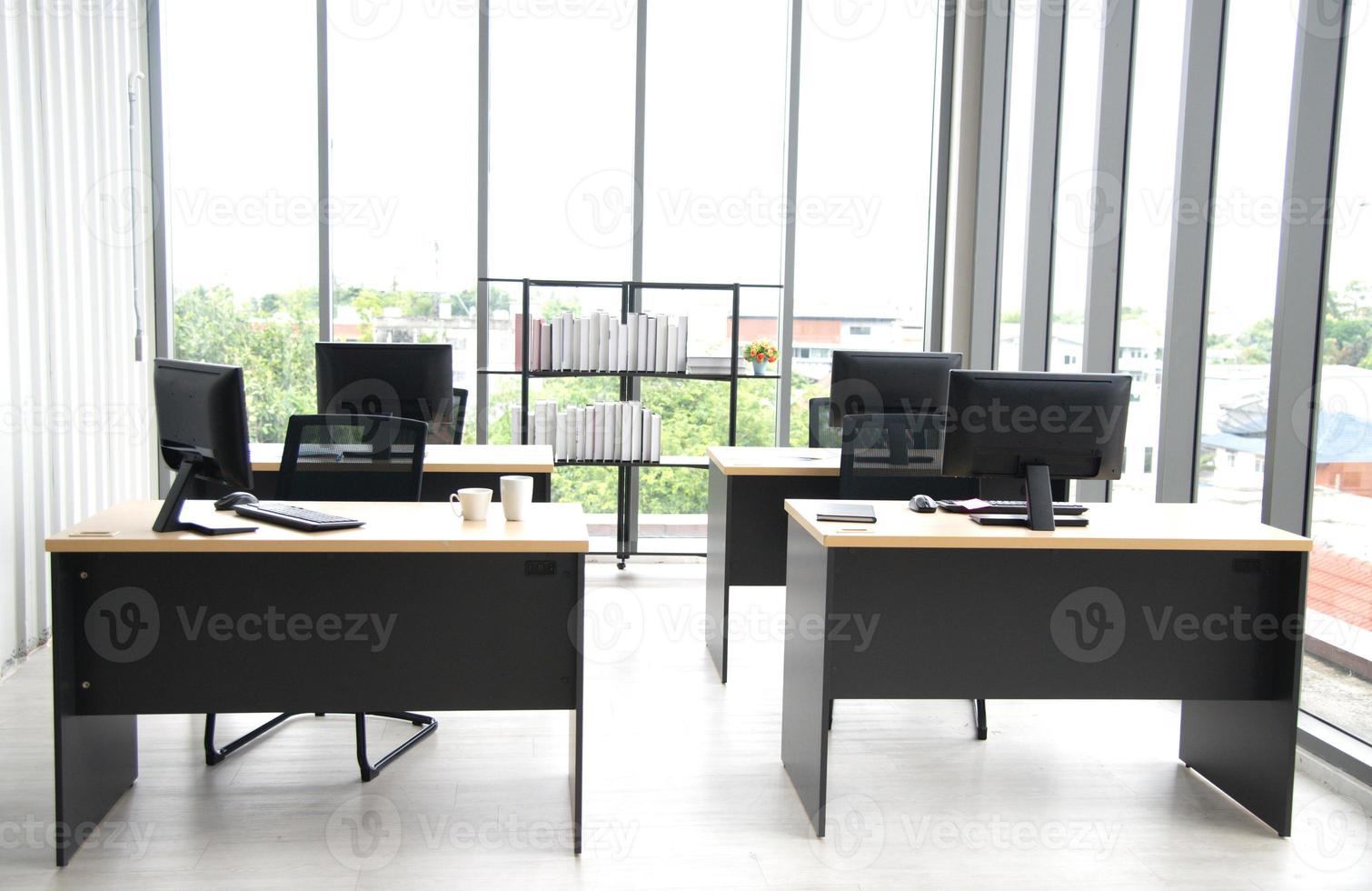 diseño de interiores de oficina moderno con mesa, computadora, monitor, gran ventana de vidrio alrededor de la habitación sin gente foto