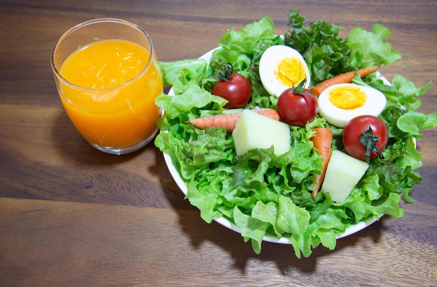 Tasty fresh mix vegetable salad on white dish and wooden plate with orange juice. photo