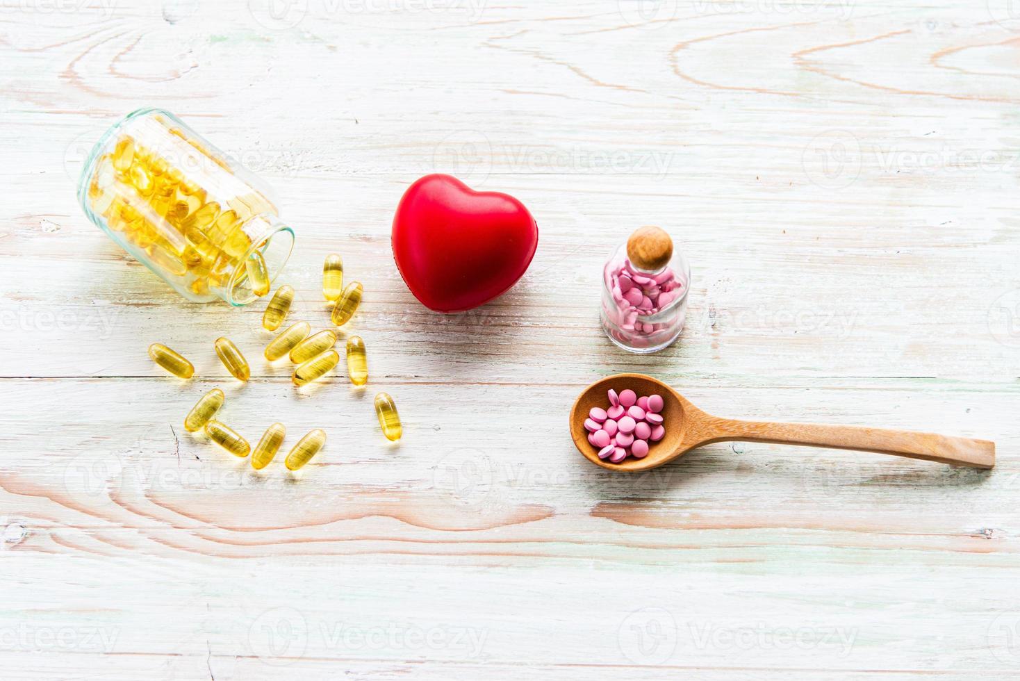 Colorful medicines in the glass bottles and wooden spoon with red heart on the wooden table. Assorted pharmaceutical medicine, vitamine, supplement pills, tablets and capsules photo