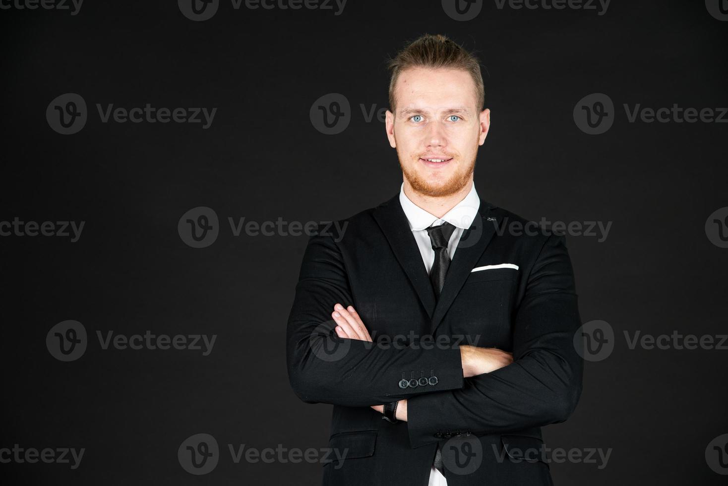 Portrait of young smart and handsome business man in black suit standing on isolated black background. photo