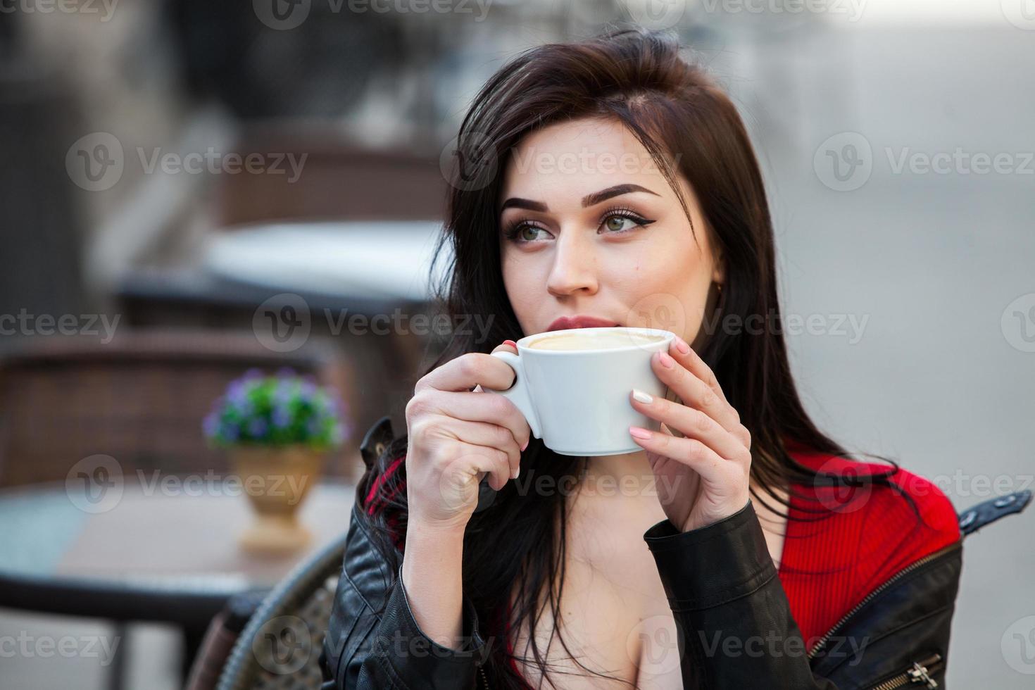 Young stylish woman drinking coffee in a city street.Stylish hipster girl drinking coffee in street. Outdoors fashion portrait of young beautiful girl drinking coffee. photo