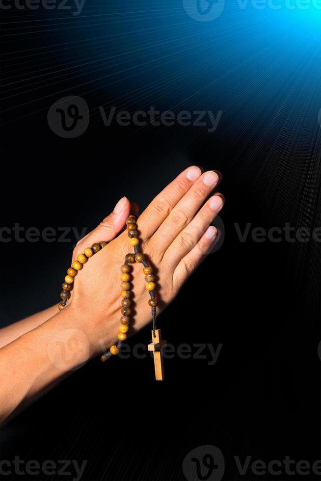 Praying Hands holding rosary beads on black background photo