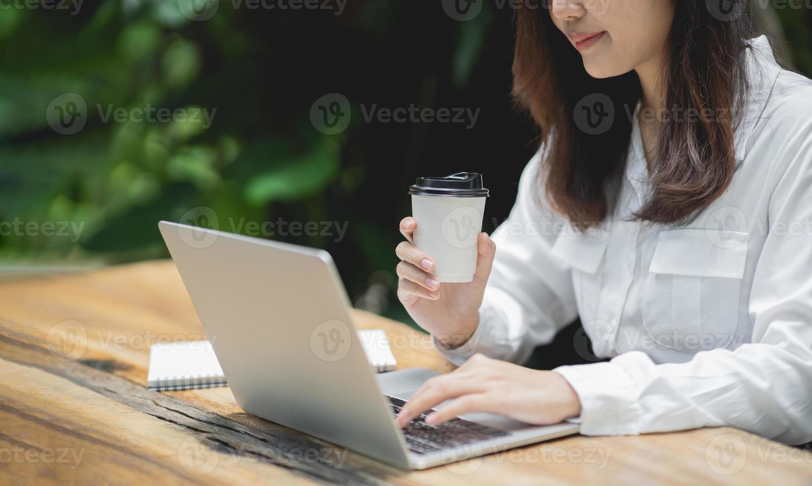 mujer de negocios trabajando en una computadora portátil y sosteniendo una taza de café caliente en una mesa de madera con una taza de café. el concepto de negocio trabaja desde casa en cualquier lugar. foto