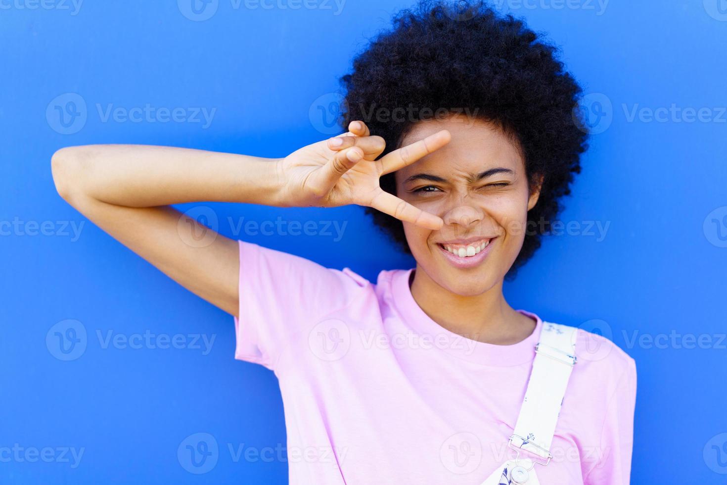 alegre mujer negra haciendo el signo de la paz cerca de la pared foto