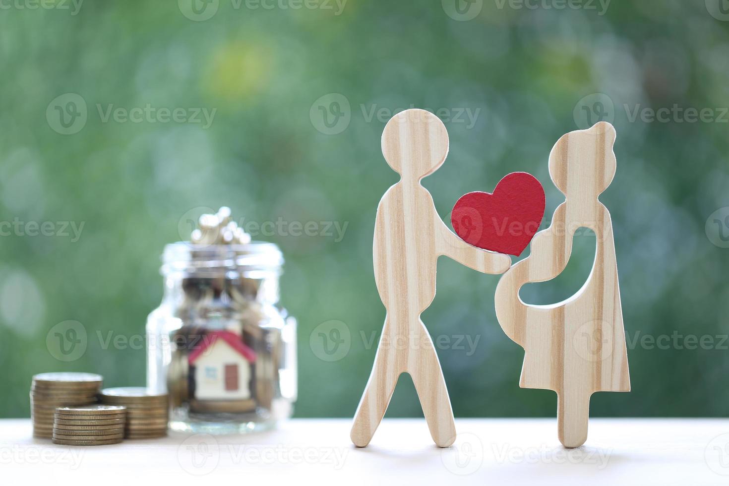 Love couple holding heart shape with model house and gold coin money in the glass bottle on natural green background,Save money for prepare in future and family finance concept photo