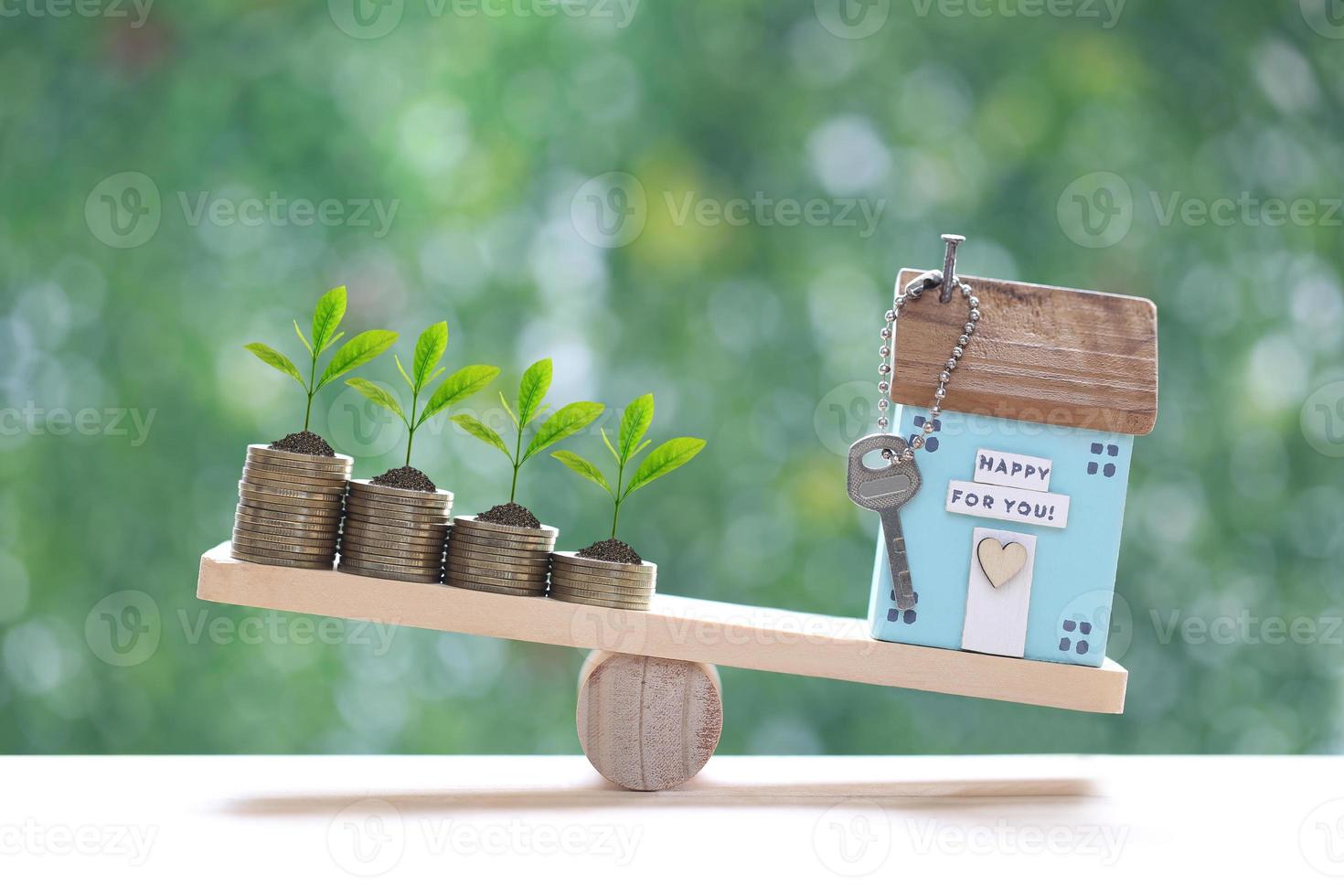 Model house with Trees growing on stack of coins money on wood scale seesaw with natural green background,Business investment and real estate concept photo