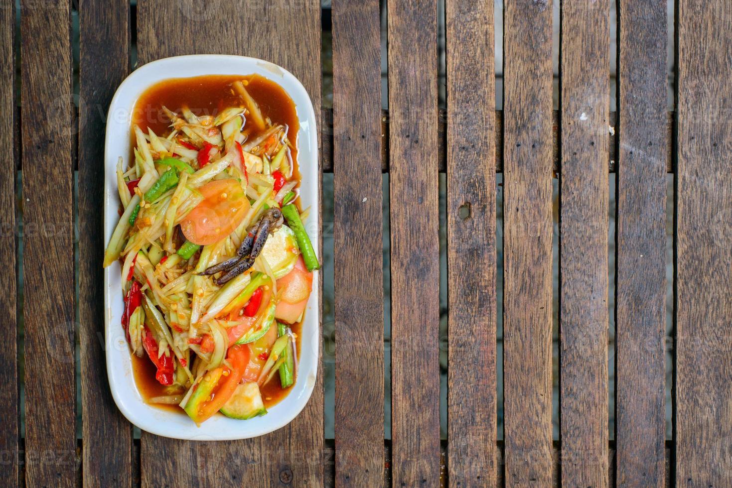 ensalada de papaya picante con cangrejo salado y pescado fermentado sobre fondo de madera. foto