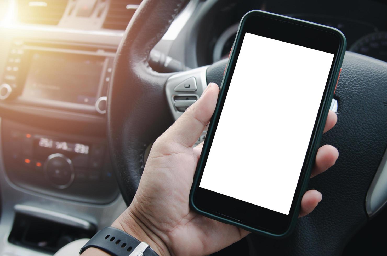 male hand holding a mobile phone in the car cabin.Blank with white screen.Mock up smart phone interior car. photo