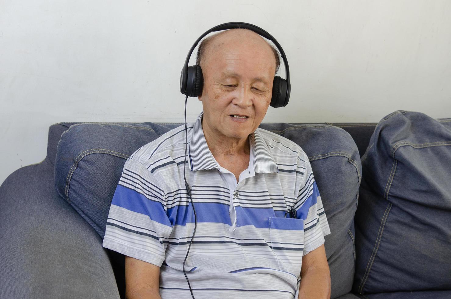 anciano escuchando música con auriculares en el sofá. foto