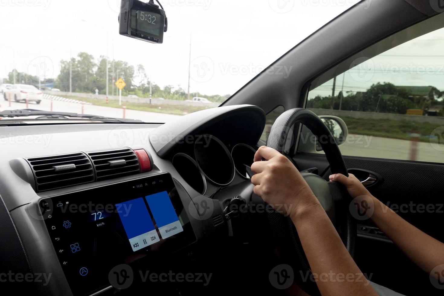 Hand of driving use car steering wheel inside the car. Third person view. Environment of asphalt on rainy time. With blurred of other cars on the road. photo