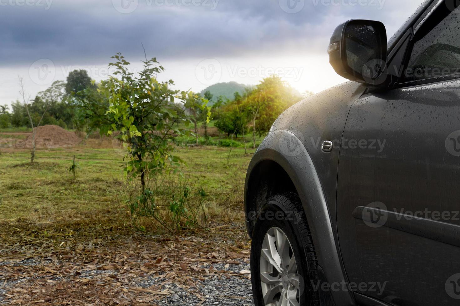 Beside of front car with drop on water on the car. Car gray color. Front side with nautre of graden green grass and trees after rainy. on the sky with dark clouds. photo