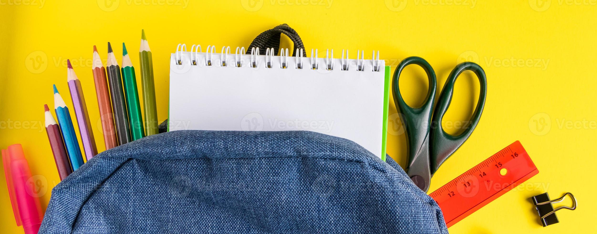 Flat lay student backpack and office supplies on yellow background. Back to school concept. Place for text. photo