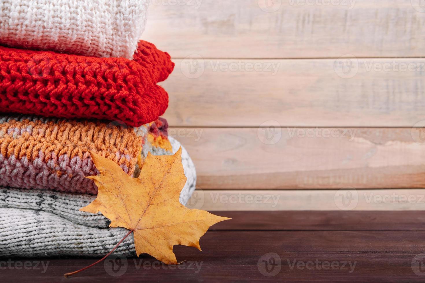 Stack of warm knitted sweaters. Autumn concept. Woolen jumpers and maple leaf on wooden background. photo