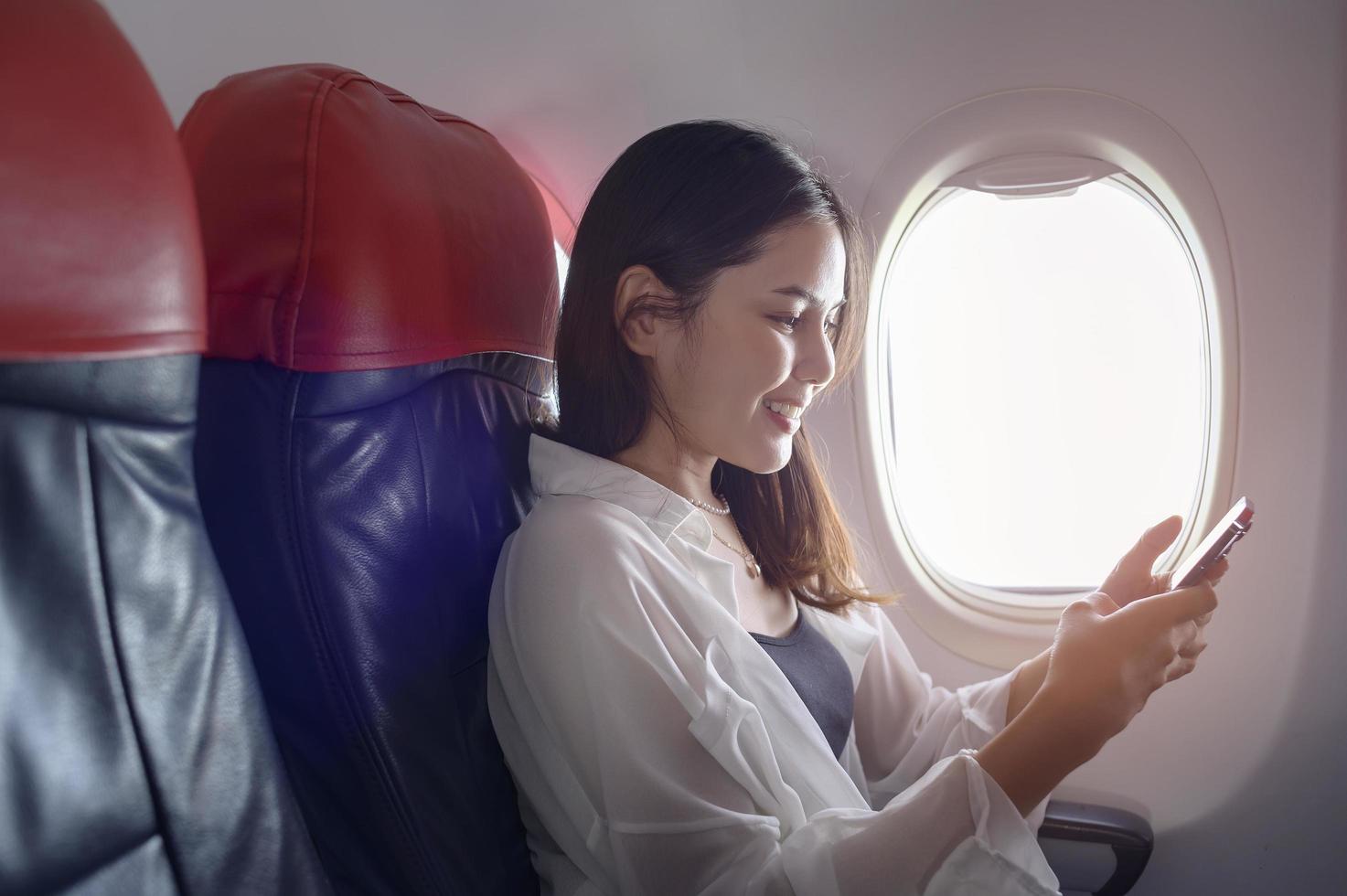 Young beautiful woman is using smartphone on airplane, travel and holidays concept photo