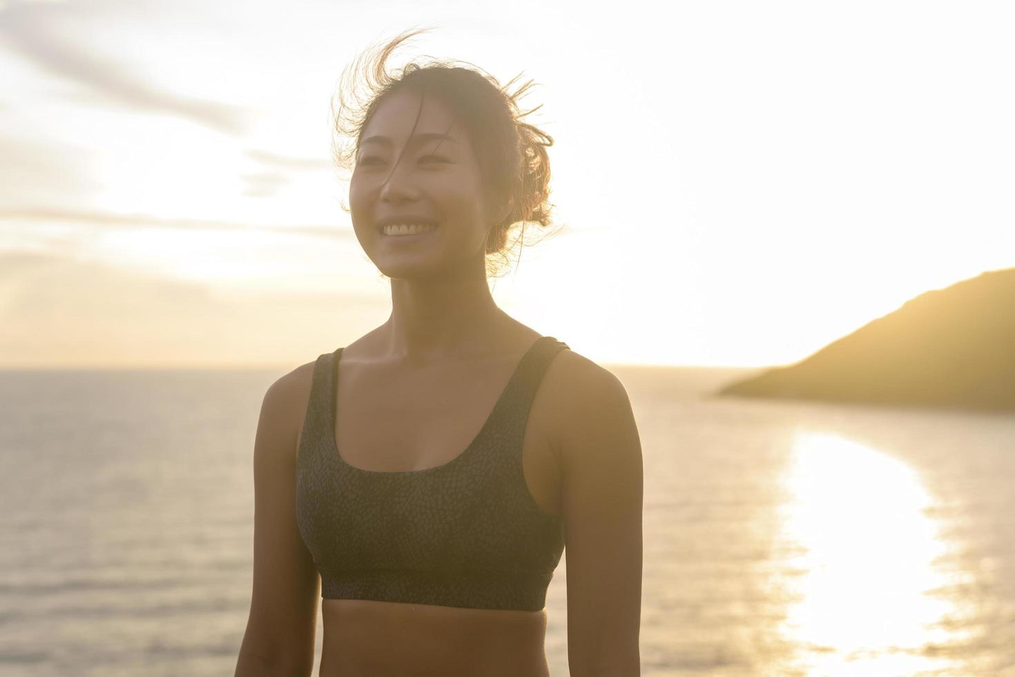 Young asian woman in sportswear doing yoga on the rock at seaside during Sunset, health and meditation concept photo