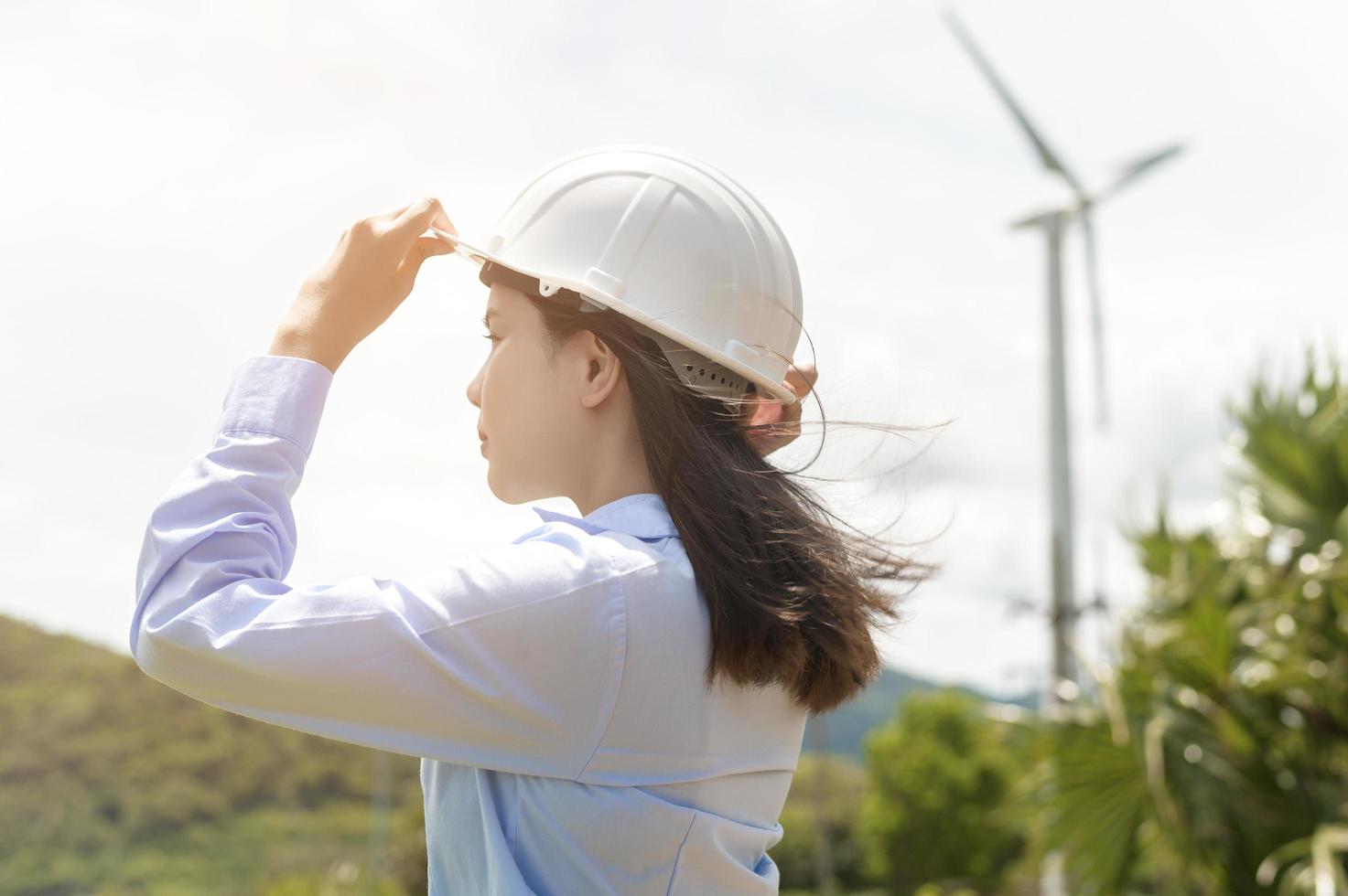 Female engineer working on the seaside wearing a protective helmet over electrical turbines background. photo